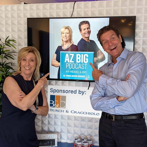 Michael & Amy in front of a picture of their podcast cover art